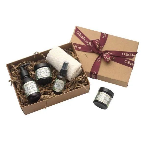 G. Baldwin & Co. Neroli and Willowbark gift box containing a face wash, clay face mask, face serum, and a soft white towel, all packaged in a brown box with a burgundy ribbon.